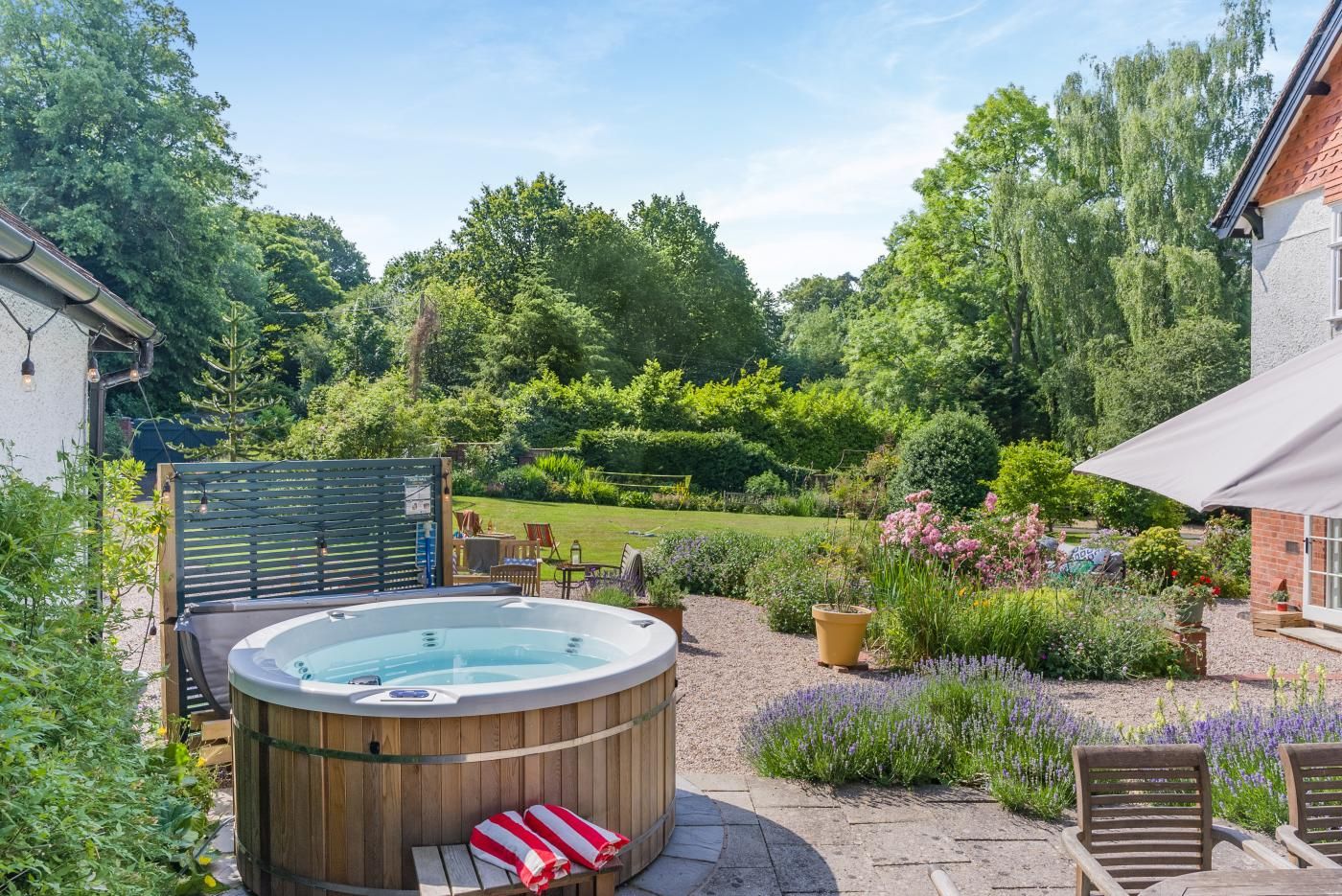 A hot tub in a garden with a wooden deck, chairs, and a patio area.