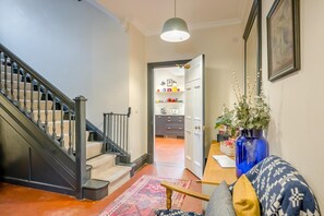 Una escalera lleva a una cocina con comedor, un jarrón azul con plantas y un cojín estampado en un sofá.