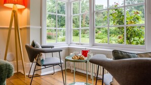 A cozy room with a bay window, a red lamp, and a table with pastries. - 5 Bed in Church Stretton (oc-t30413) (Church Stretton)