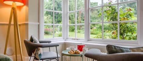 Una habitación acogedora con un ventanal, una lámpara roja y una mesa con pasteles.