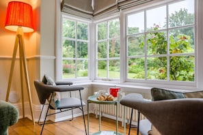Una habitación acogedora con un ventanal, una lámpara roja y una mesa con pasteles.