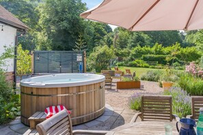 A wooden hot tub with seating, surrounded by a garden with various plants and a lawn. - 5 Bed in Church Stretton (oc-t30413) (Church Stretton)