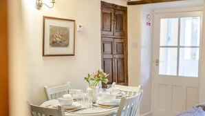 Un coin repas avec une table ronde dressée pour quatre personnes, des chaises blanches, un vase avec des fleurs et un tableau encadré au mur.