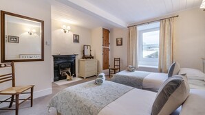 Une chambre d’hôtel avec deux lits, une cheminée, une commode, une chaise et une grande fenêtre avec des rideaux.