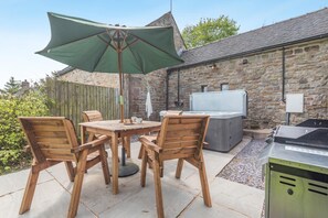 Eine Terrasse mit Holztisch und Stühlen, einem grünen Sonnenschirm, einer Steinmauer und einem Grill.