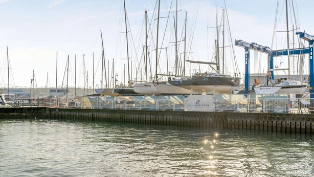 A marina with multiple sailboats docked, a crane, and a building with signage. - 2 Bed in East Cowes (oc-h30421) (East Cowes)
