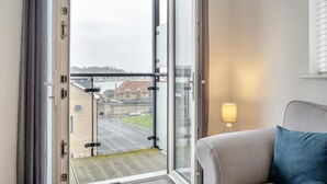 A hotel room with a large sliding glass door leading to a balcony, a sofa with a blue pillow, and a table lamp. - 2 Bed in East Cowes (oc-h30421) (East Cowes)