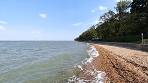 A beach with pebbles, a clear sky, and a forested area. - 2 Bed in East Cowes (oc-h30421) (East Cowes)
