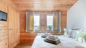 Ein Zimmer mit Holzwandverkleidung, einem Bett, zwei Vorhängen und einem an der Wand befestigten Fernseher sowie einem Heizkörper.