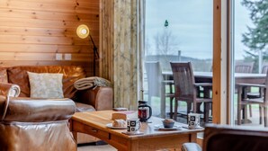 Ein gemütliches Zimmer mit Holzvertäfelung, einem Ledersofa, einem Esstisch mit Stühlen und Blick ins Freie.