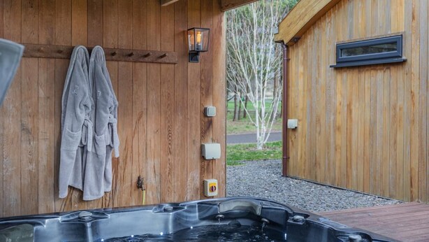 Ett spa-rum i trä med ett bubbelbad, handdukar och utsikt över träd.