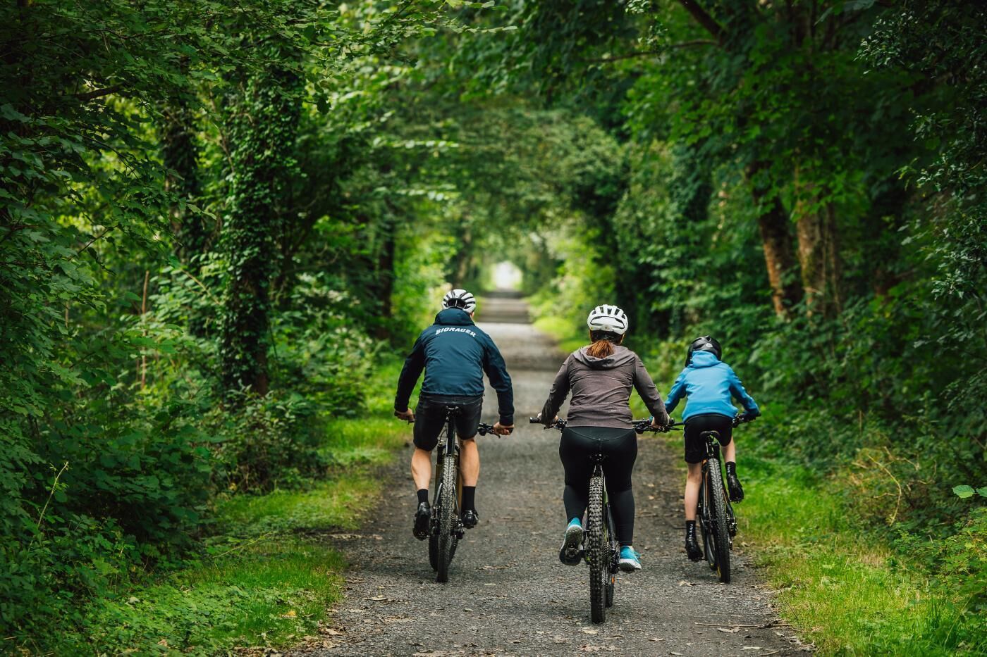 Trois cyclistes sur un sentier étroit bordé d’arbres.