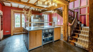 A kitchen with wooden beams, a stainless steel island, and a staircase with striped carpet.