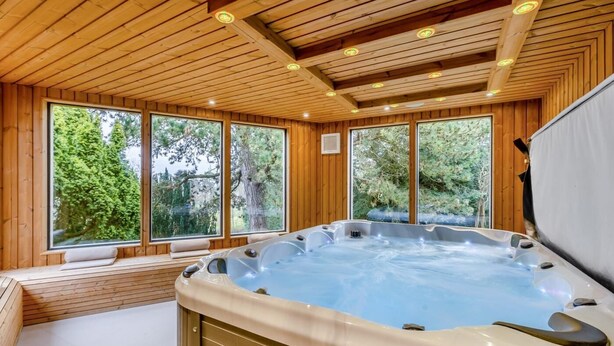 A wooden cabin with a hot tub, large windows, and a view of trees.