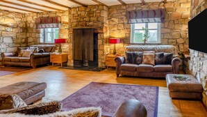 A cozy living room with stone walls, a fireplace, leather sofas, and a flat-screen TV.