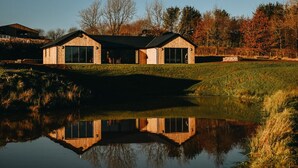 A modern house with a large glass window, a wooden deck, and a pond in front. - 3 Bed in Merthyr Cynog (oc-g30312) (Brecon)