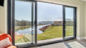 A modern room with a sliding glass door leading to a view of a river and a grassy area. - 3 Bed in Merthyr Cynog (oc-g30312) (Brecon)