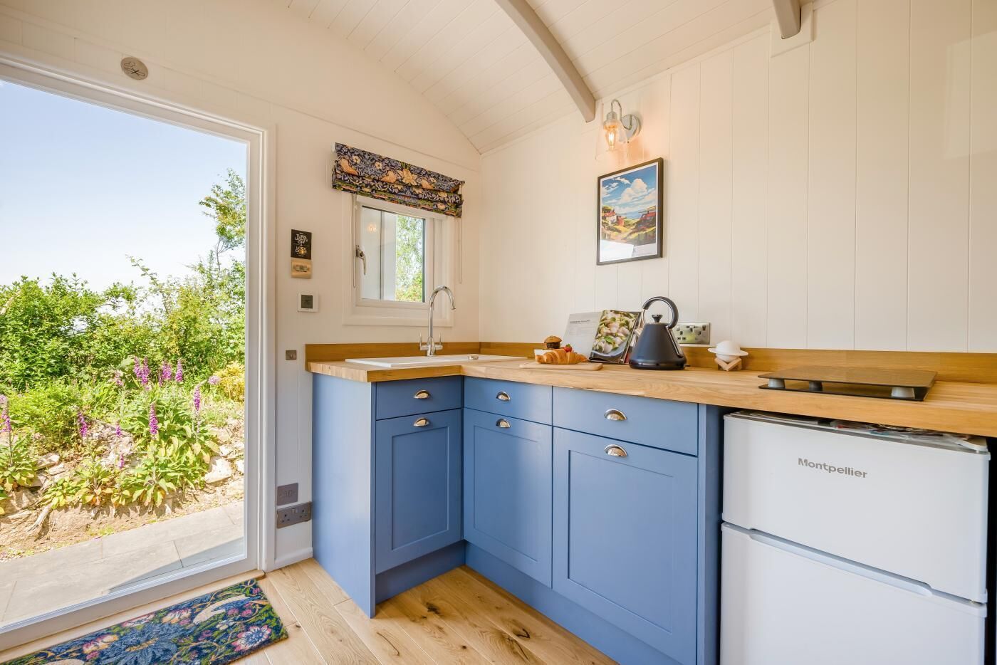 A kitchen with blue cabinets, a white refrigerator, and a window with a view of greenery.
