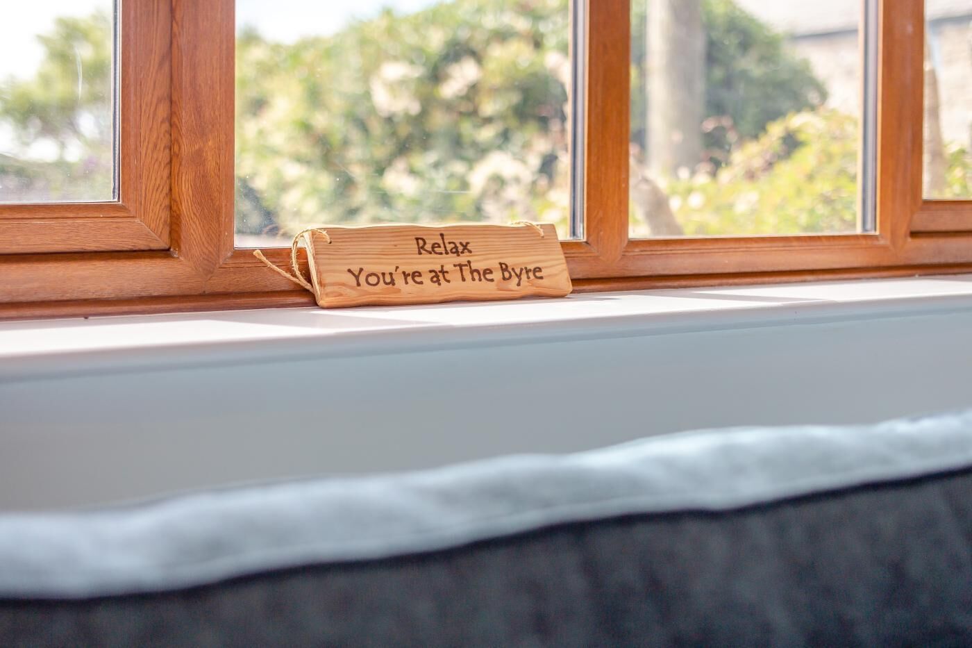 Ein Holzschild mit dem Text "Relax You're at The Bye“ auf einem Fensterbrett.