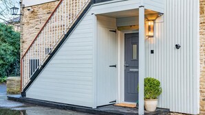 A white wooden staircase leading to a door with a small porch area, a potted plant, and a stone wall. - 1 Bed in Skipton (oc-w30426) (Skipton)