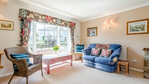 A living room with a blue sofa, wicker chairs, a coffee table, and a window with curtains. - 3 Bed in Hawes (oc-s30429) (Hawes)