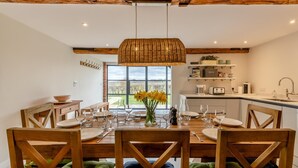 Comedor con mesa de madera preparada para seis personas, lámpara colgante de mimbre y vista al exterior a través de un amplio ventanal.
