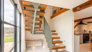 Una escalera moderna con escalones de madera y barandillas de metal, que conduce a una zona de cocina con horno y microondas integrados.