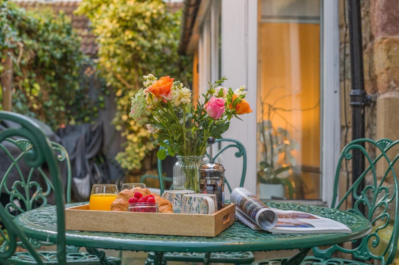 A table with a tray of croissants, a glass of orange juice, and a vase with flowers.