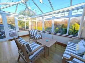 A conservatory with a wooden floor, a table, two striped sofas, and a chair. - 2 Bed in Brighstone (oc-n30464) (Brighstone)