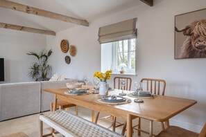 A dining area with a wooden table set for four, a bench, and a sofa in the background. - 3 Bed in Whitwell (oc-d30478) (Godshill)