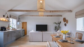 A modern kitchen with a dining area, featuring a wooden ceiling, a flat-screen TV, and a dining table set for four. - 3 Bed in Whitwell (oc-d30478) (Godshill)