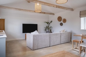 A modern living room with a grey sofa, a flat-screen TV, a wooden ceiling, and a woven light fixture. - 3 Bed in Whitwell (oc-d30478) (Godshill)