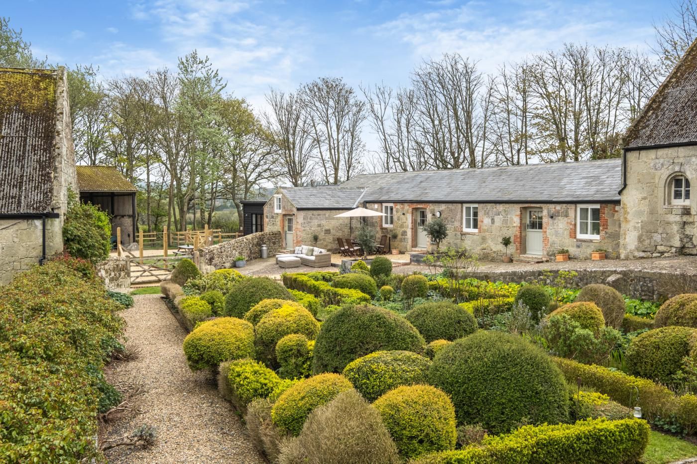 A stone building with a thatched roof, surrounded by a well-maintained garden with neatly trimmed hedges.