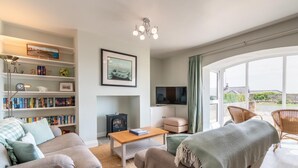 A modern living room with a sofa, a coffee table, a bookshelf, a fireplace, a TV, and a balcony with wicker chairs. - 2 Bed in Beadnell (oc-f30468) (Beadnell)