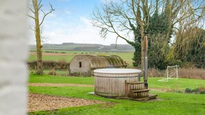 A rustic outdoor hot tub in a grassy area with a wooden structure and a metal heater in the background. - 6 Bed in Rudston (oc-s30441) (Rudston)