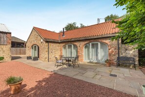 A stone building with a tiled roof, a patio with a table and chairs, and a bench. - 1 Bed in Crakehall (oc-o30357) (Kirkbridge)