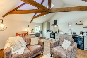Un espace de vie de style loft avec des poutres apparentes, une kitchenette, un coin repas et un espace buanderie.