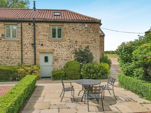 Une maison en pierre avec un toit en tuiles, une porte d’entrée et un petit jardin agrémenté d’une table et de chaises.