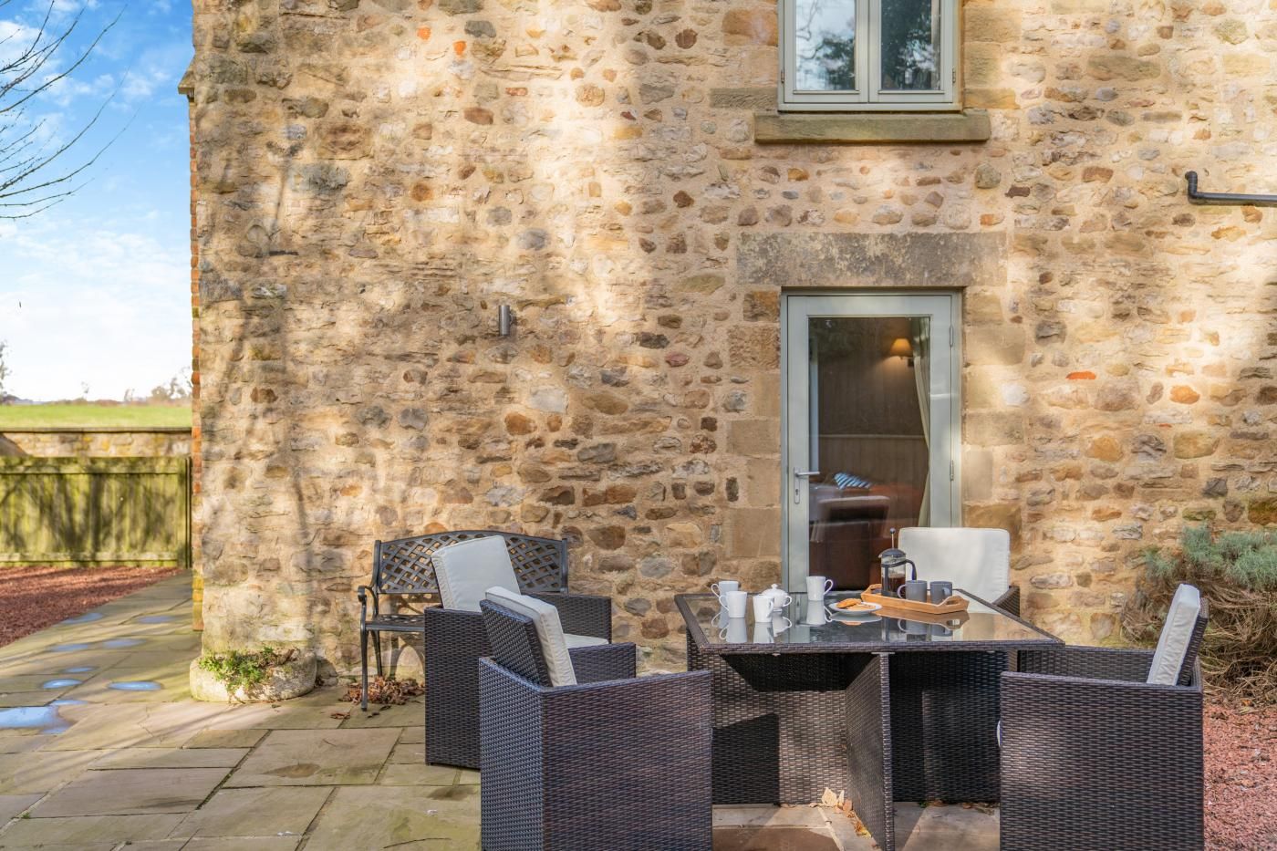 A stone building with a glass door entrance, wicker furniture, and a table set for dining.