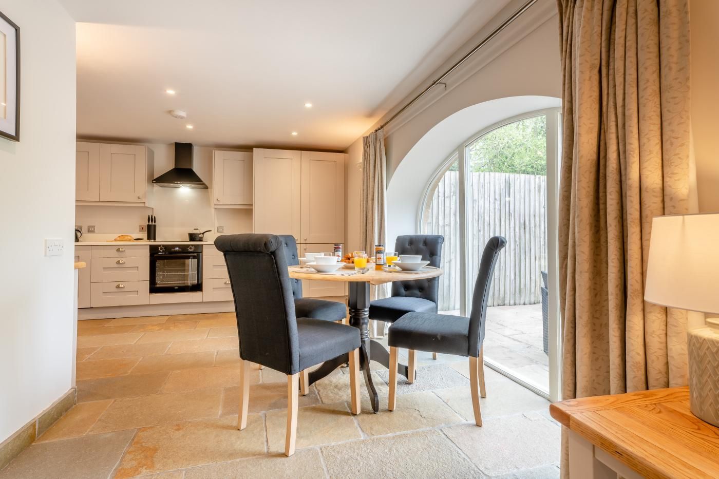 A modern kitchen with white cabinets, a dining table with four chairs, and a large window with curtains.