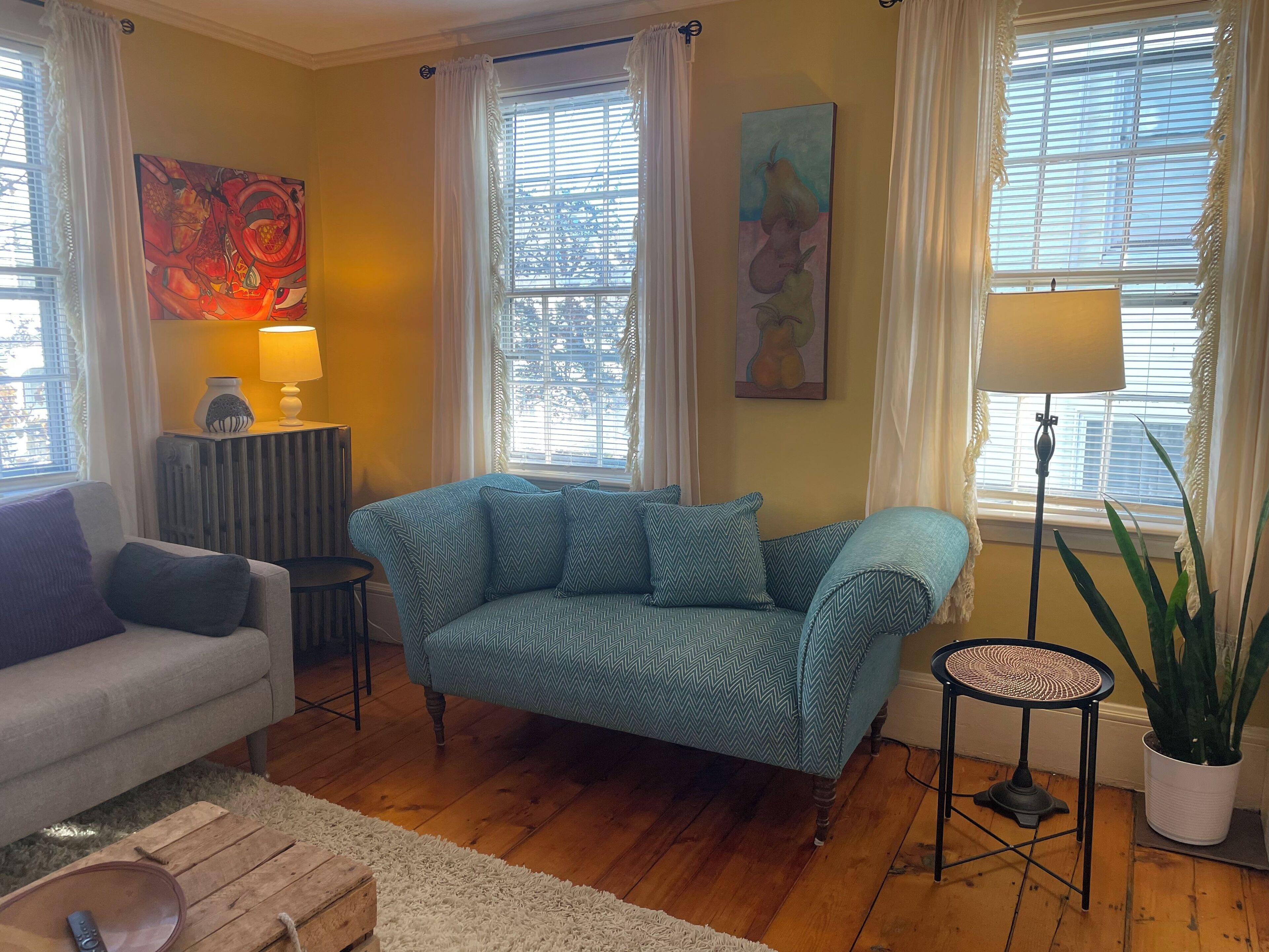 Una sala de estar con un sofá azul, un sillón gris, una mesita y una planta en maceta.