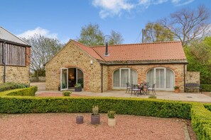 A stone building with a tiled roof, a patio with a table and chairs, and a well-maintained garden. - 2 Bed in Crakehall (oc-b30354) (Kirkbridge)