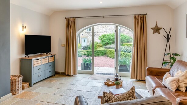 Sala de estar com televisão, sofá, mesa de centro e vista para um jardim através de uma porta de vidro.