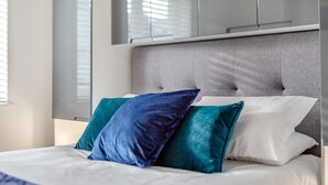 Een net opgemaakt bed met een grijs hoofdbord, witte en teal kussens en een witte dekbed.