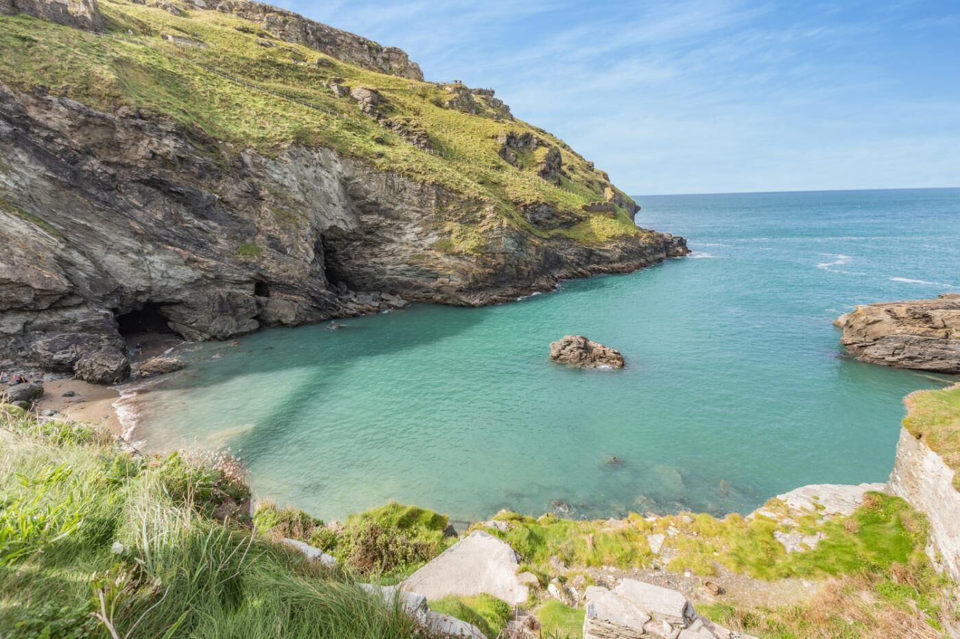 A coastal landscape with rocky cliffs, clear turquoise waters, and grassy terrain.