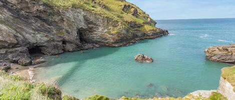A coastal landscape with rocky cliffs, clear turquoise waters, and grassy terrain.
