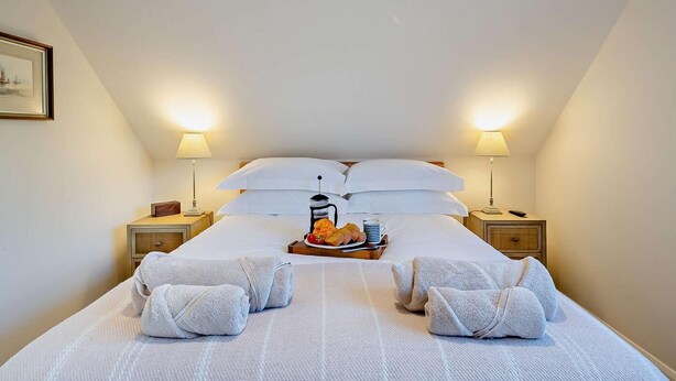Een net opgemaakt bed met witte lakens, twee nachtkastjes met lampen, en een dienblad met ontbijtartikelen.