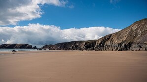 En bred sandstrand med klippestykker i baggrunden og en klar blå himmel.