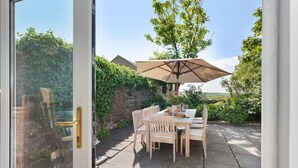 En patio med et bord, stole og en parasol, samt en stenvæg.