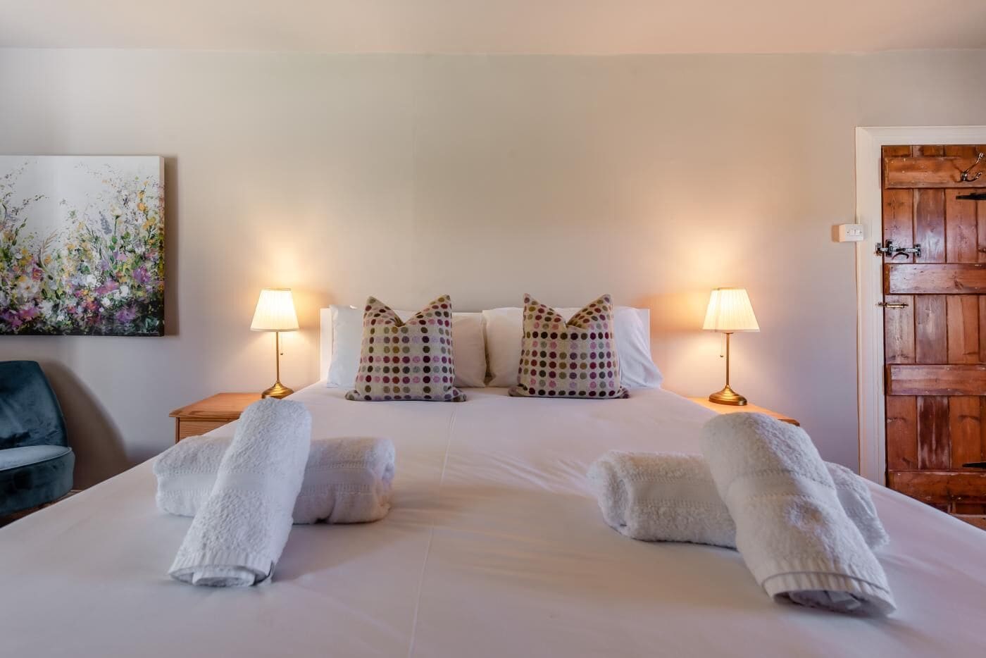 A neatly made bed with white linens, two pillows with polka dots, two bedside lamps, and a wooden door.